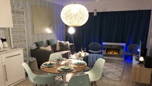 En moderne stue med et rundt spisebord, lyseblå stole, en pejs og en stor hængende lampe.