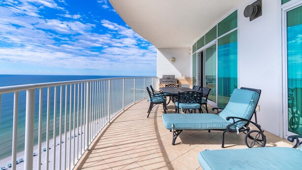 A balcony with a view of the ocean, a table with chairs, and a grill.
