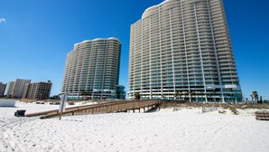 Two high-rise hotels with balconies, a sandy beach, and a wooden boardwalk.