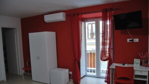 A room with a white wardrobe, a small white heater, a red chair, a desk, and a TV mounted on the wall. - Sorrento deluxe Balcony (Sorrento)