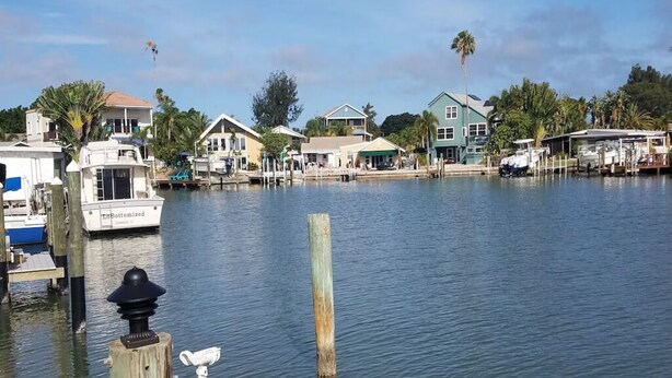 Un port de plaisance avec des bateaux amarrés, des maisons au bord de l’eau et une étendue d’eau calme.