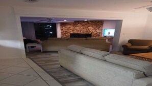 Un salon avec un grand canapé gris, un mur décoratif en pierre, un téléviseur à écran plat et un ventilateur de plafond.
