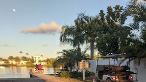 Une voiturette de golf est garée au bord d’un sentier qui longe le rivage, avec des palmiers et un panneau indicateur à proximité.