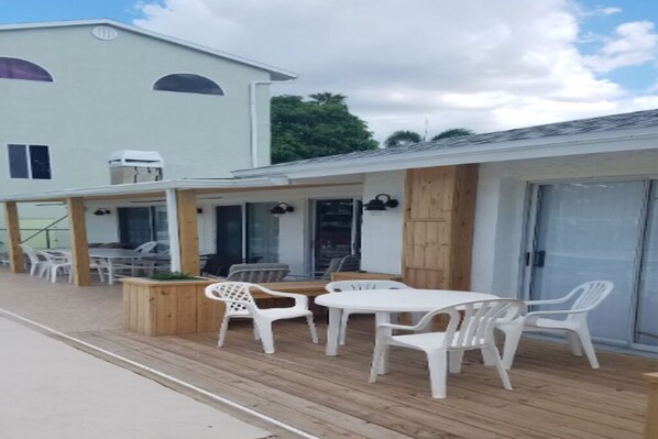 An outdoor patio with a wooden deck, white plastic chairs, and a table.