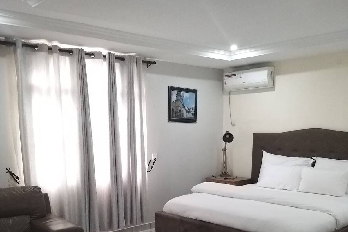 A modern hotel room with a large bed, a sofa, a coffee table, and a picture on the wall.
