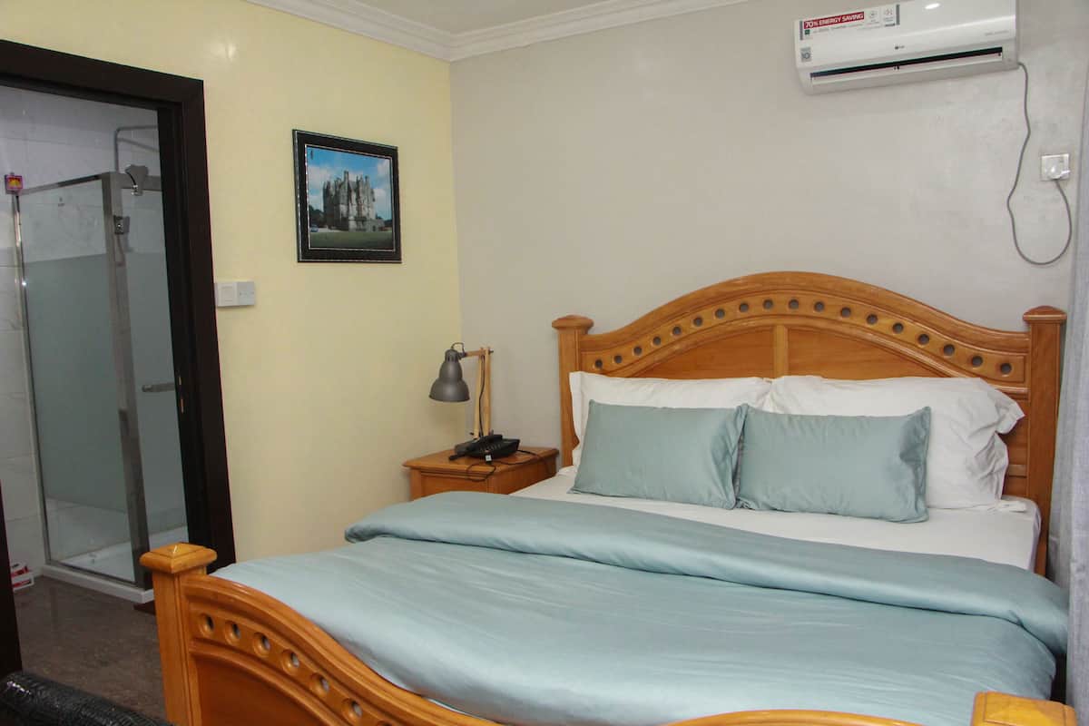 A bedroom with a wooden bed, a bedside table with a lamp, and a wall-mounted air conditioner.