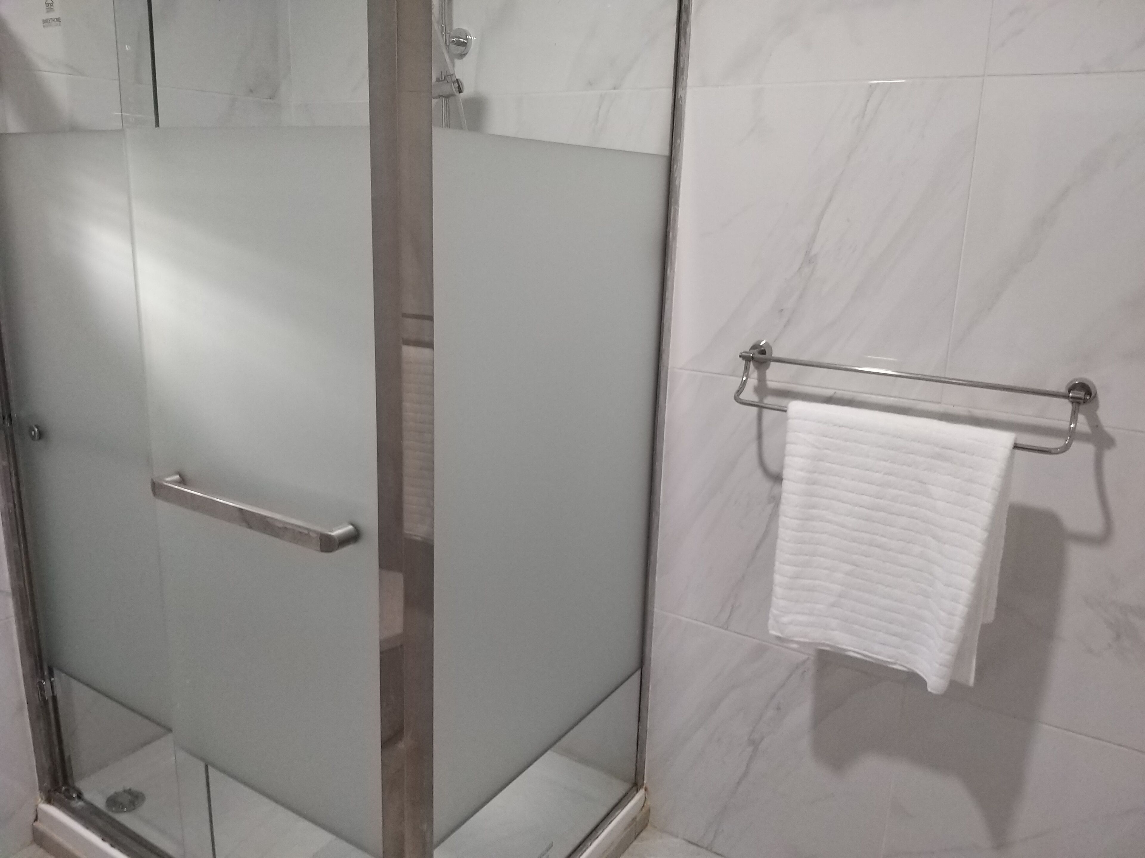 Une salle de bain avec une douche à parois de verre, un porte-serviettes avec une serviette blanche et des carreaux de marbre.