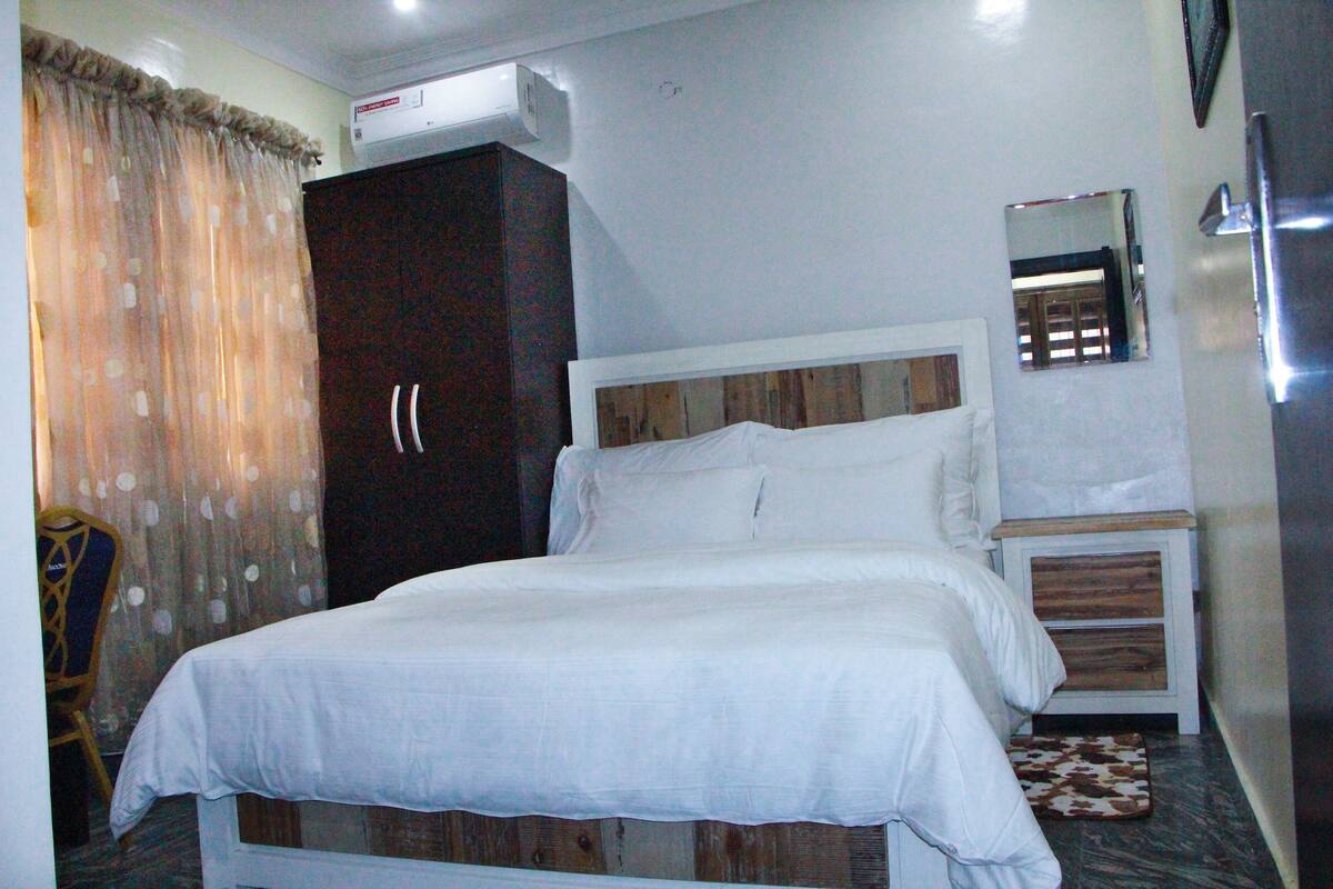 A bedroom with a bed, a wardrobe, a mirror, and a small wooden side table.