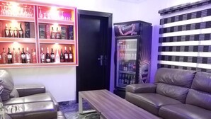 A bar area with shelves of liquor bottles, a refrigerator with a Williams Dark Ale sign, and leather seating. - Mitos Luxury Suites (Lagos)
