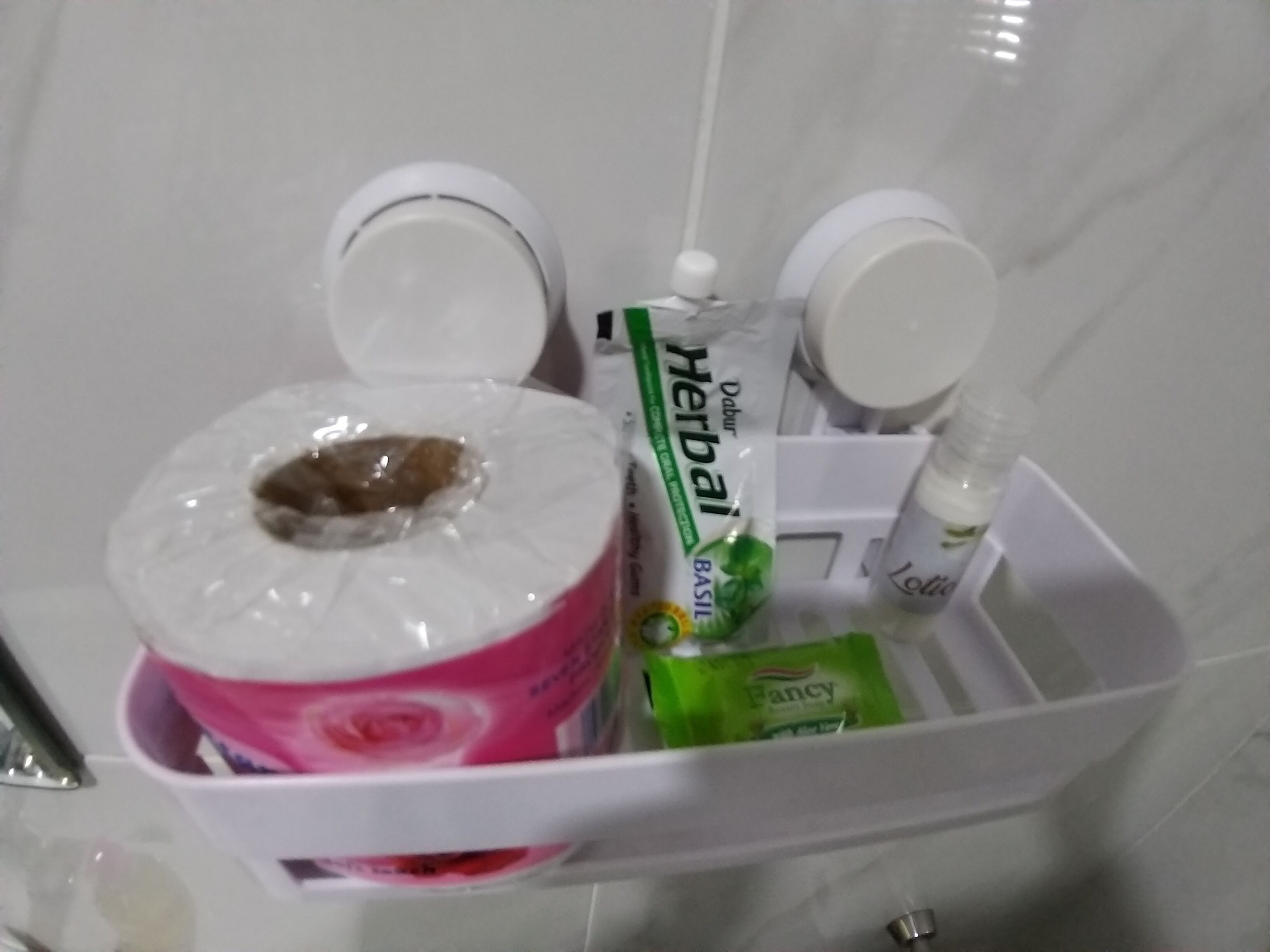 A bathroom with a white sink, a mirror, and a white storage basket containing a pink bottle, a green packet, and a white bottle.