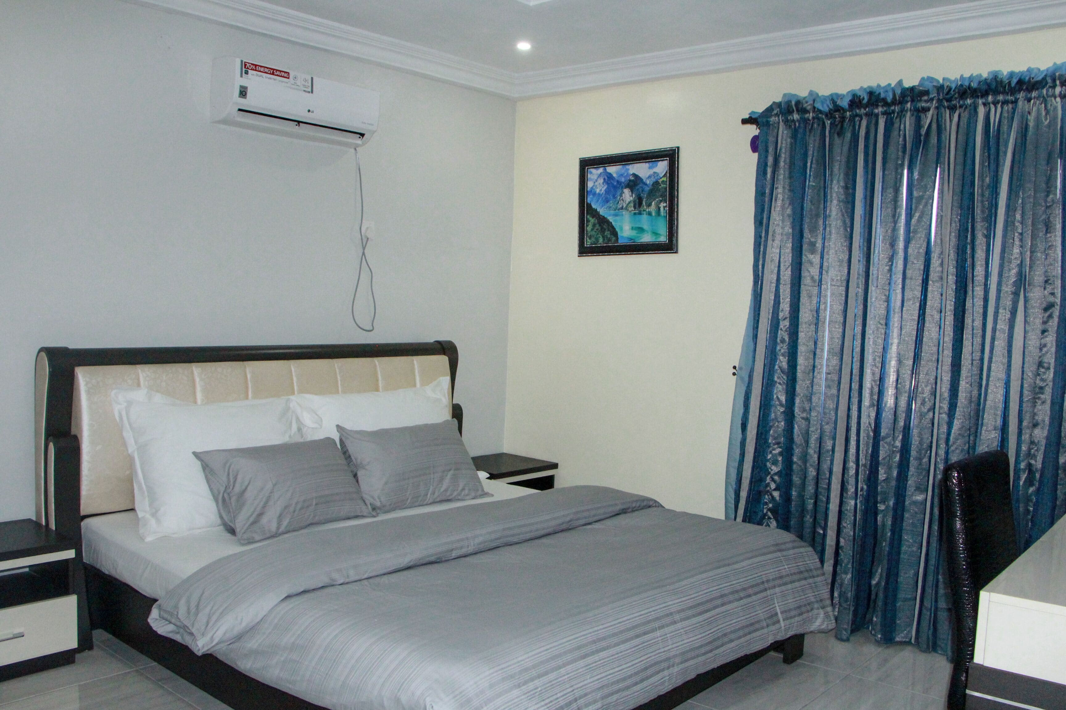 Een slaapkamer met een bed, nachtkastjes, een airconditioningapparaat, een ingelijst beeld aan de muur en een gordijn.