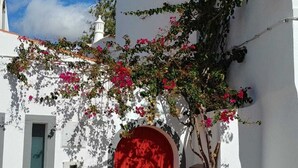 A white building with a red door, a small window, and a chimney.