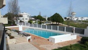 A swimming pool with a white fence, a grassy area, and a building in the background.