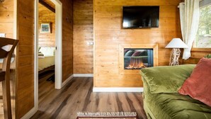 Interior d'una cabana acollidora amb un terra de fusta, un sofà verd, una llar de foc i un televisor fixat a la paret.