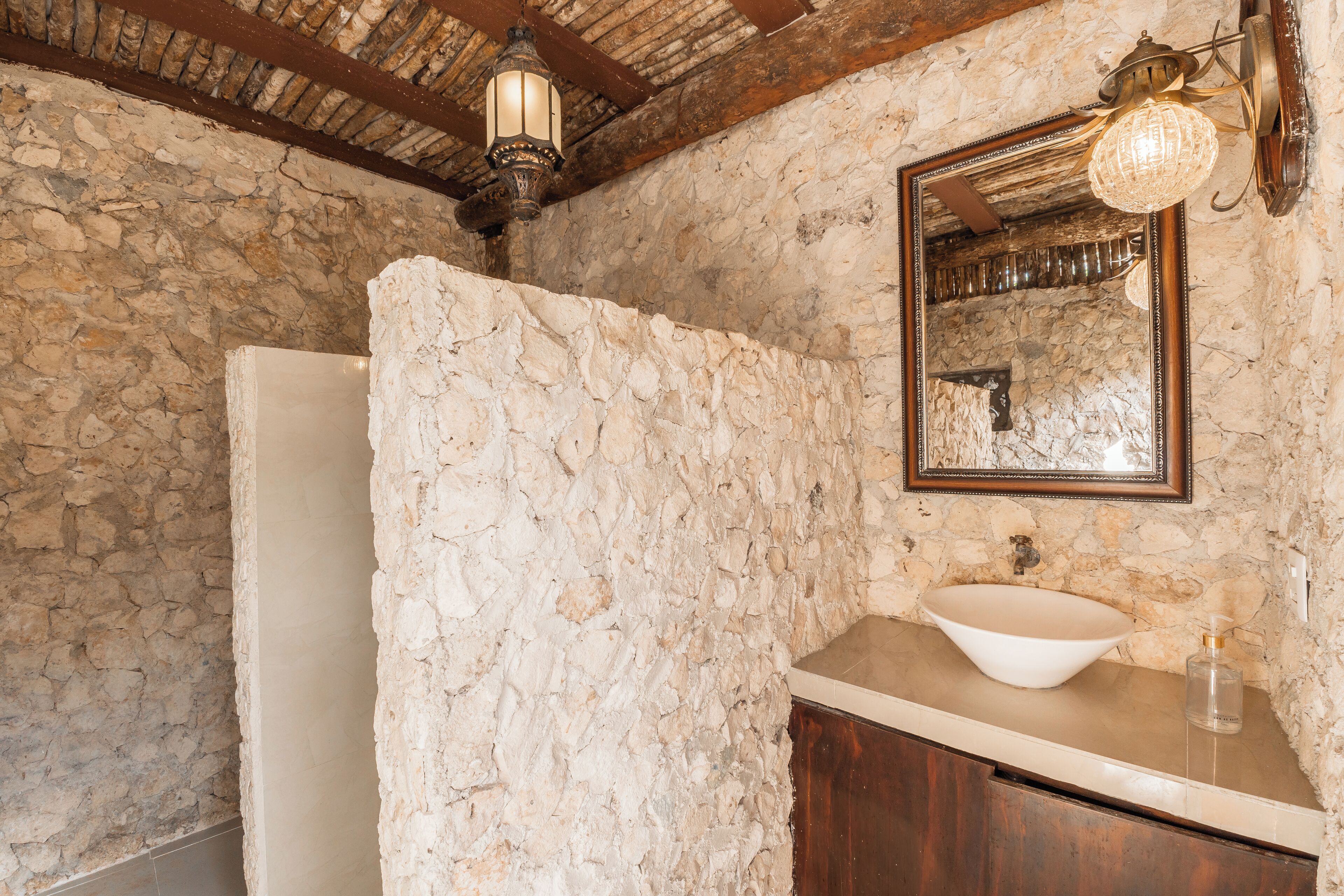 A bathroom with a stone wall, a white sink, and a wooden cabinet.