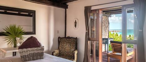 Un dormitorio con una cama, una silla, una planta y vista al océano a través de un ventanal corredera.