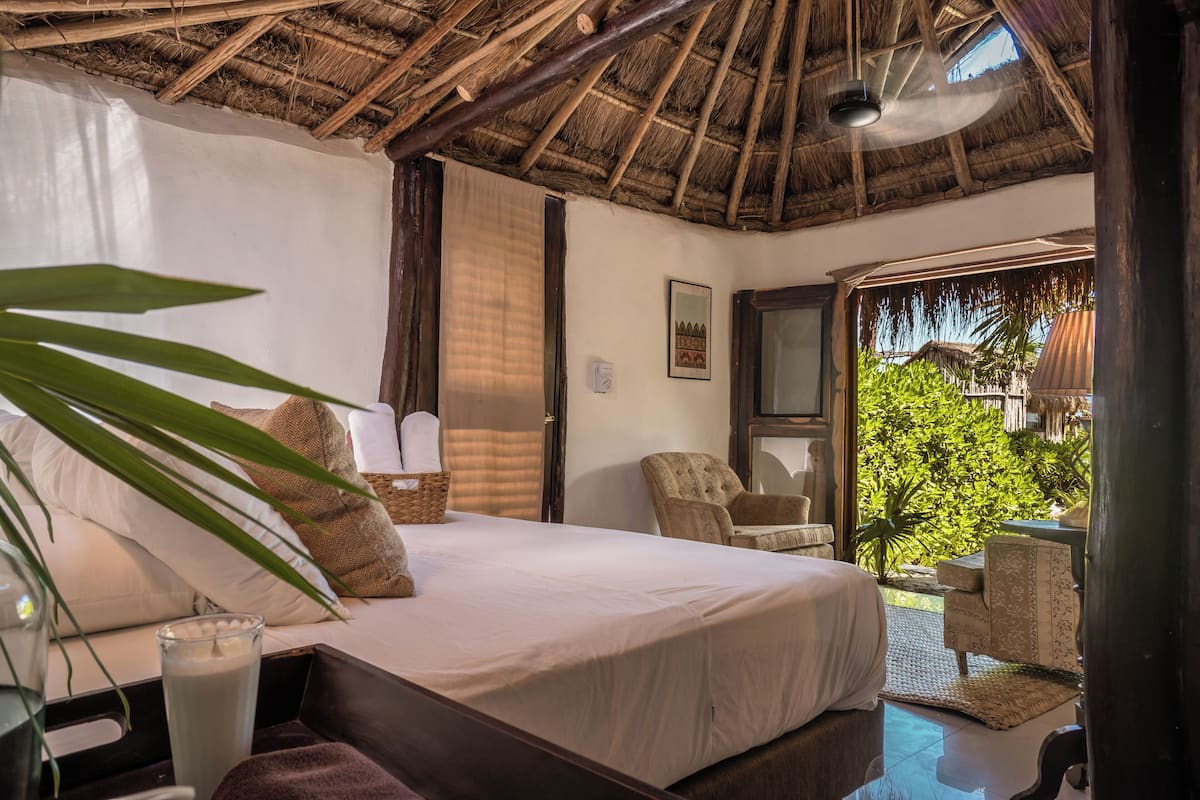 A bedroom with a bed, bedside table, and a view of a lush garden.