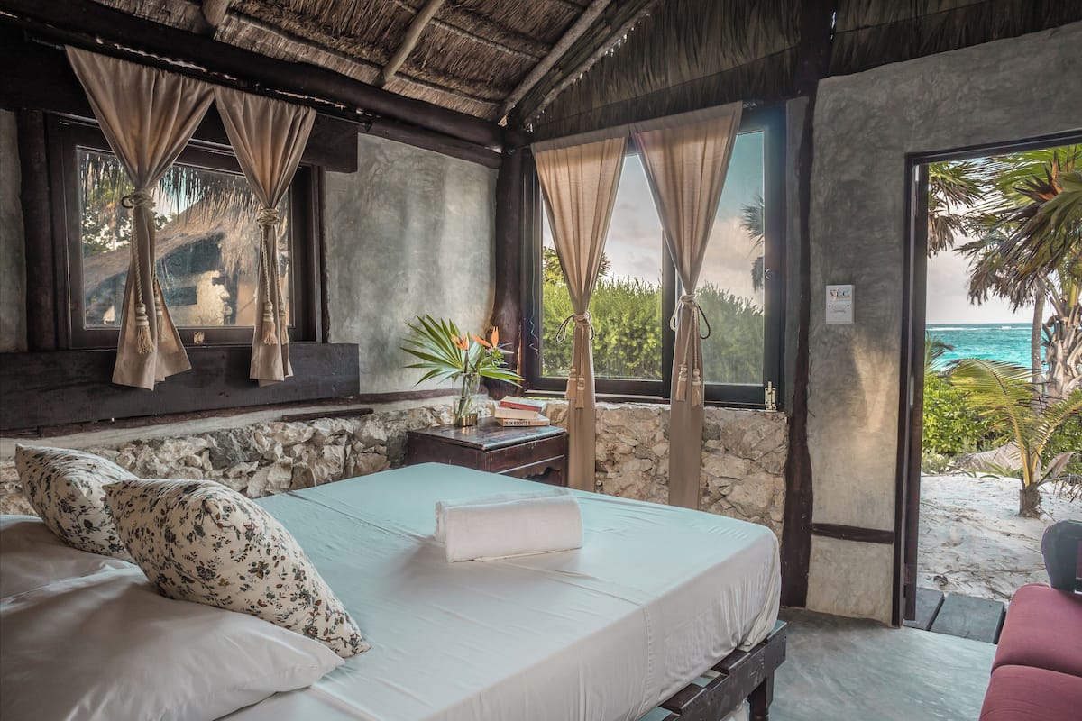 A bedroom with a bed, a nightstand, a potted plant, and a view of the beach.