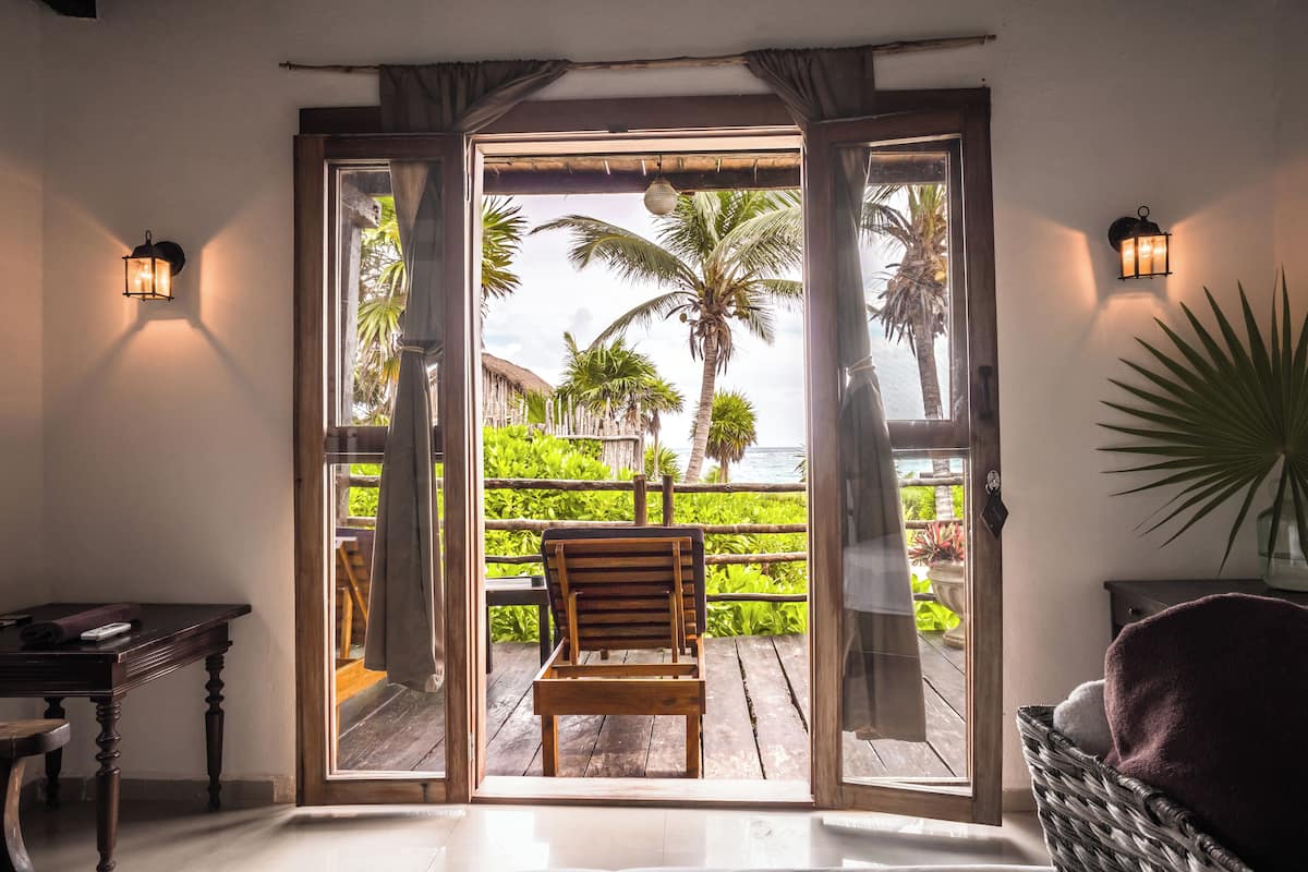 A wooden chair on a balcony with a view of palm trees and a beach.