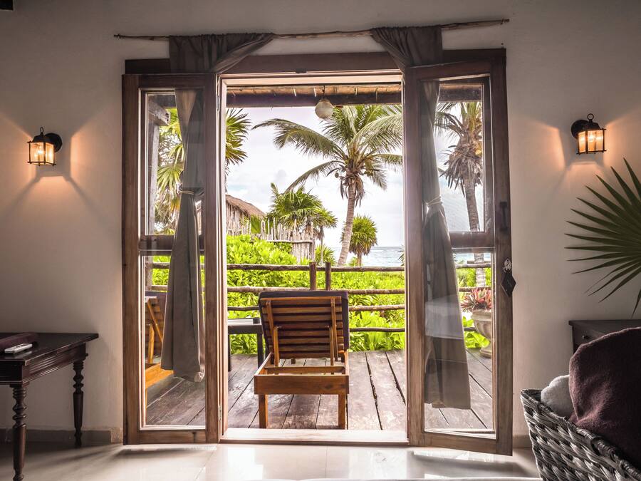 Une chaise en bois sur un balcon, avec vue sur des palmiers et une plage.