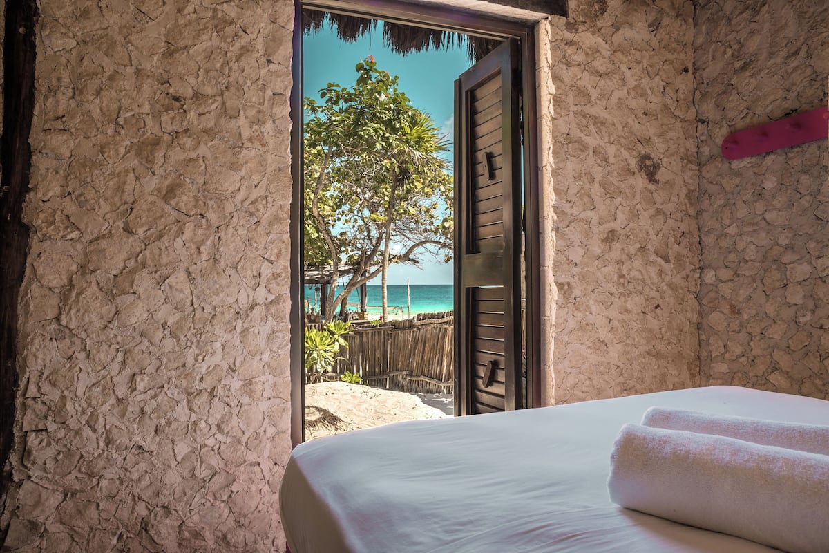 A room with a bed, a view of the beach, and a wooden door.