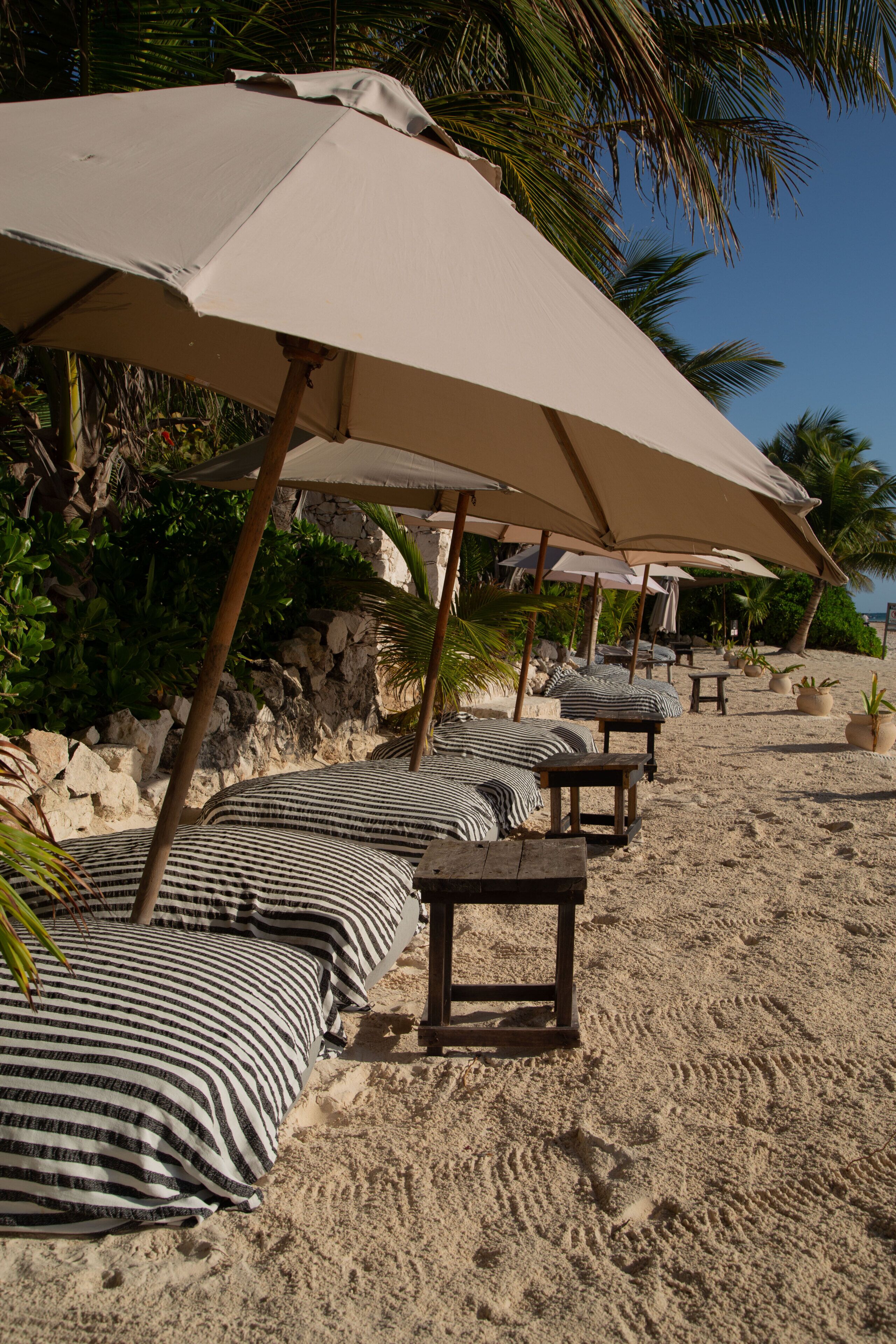 Een strandsetting met meerdere parasols, gestreepte kussens en houten tafels.