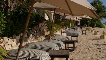 Een strandsetting met meerdere parasols, gestreepte kussens en houten tafels.