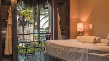 Una habitación con una cama, una mesita de noche, una lámpara y vistas a una palmera a través de una puerta abierta.