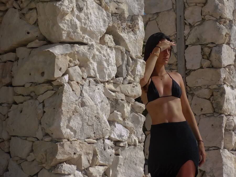 Una persona de pie frente a un muro de piedra con una reja metálica.