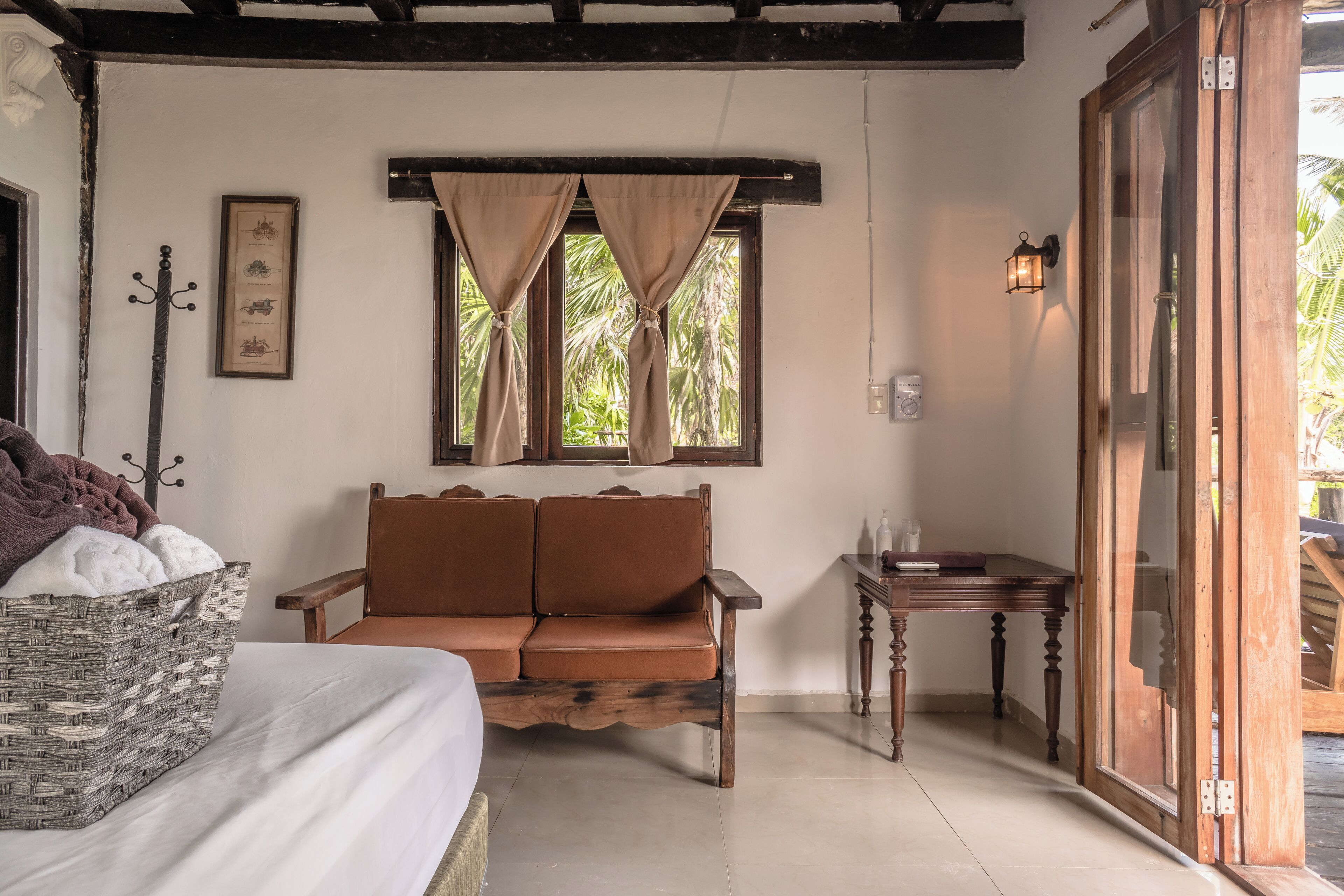 A room with a bed, a brown sofa, a small table, a window with curtains, and a wooden door.