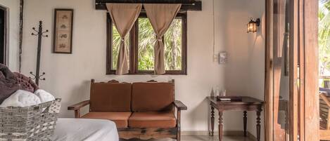 A room with a bed, a brown sofa, a small table, a window with curtains, and a wooden door.