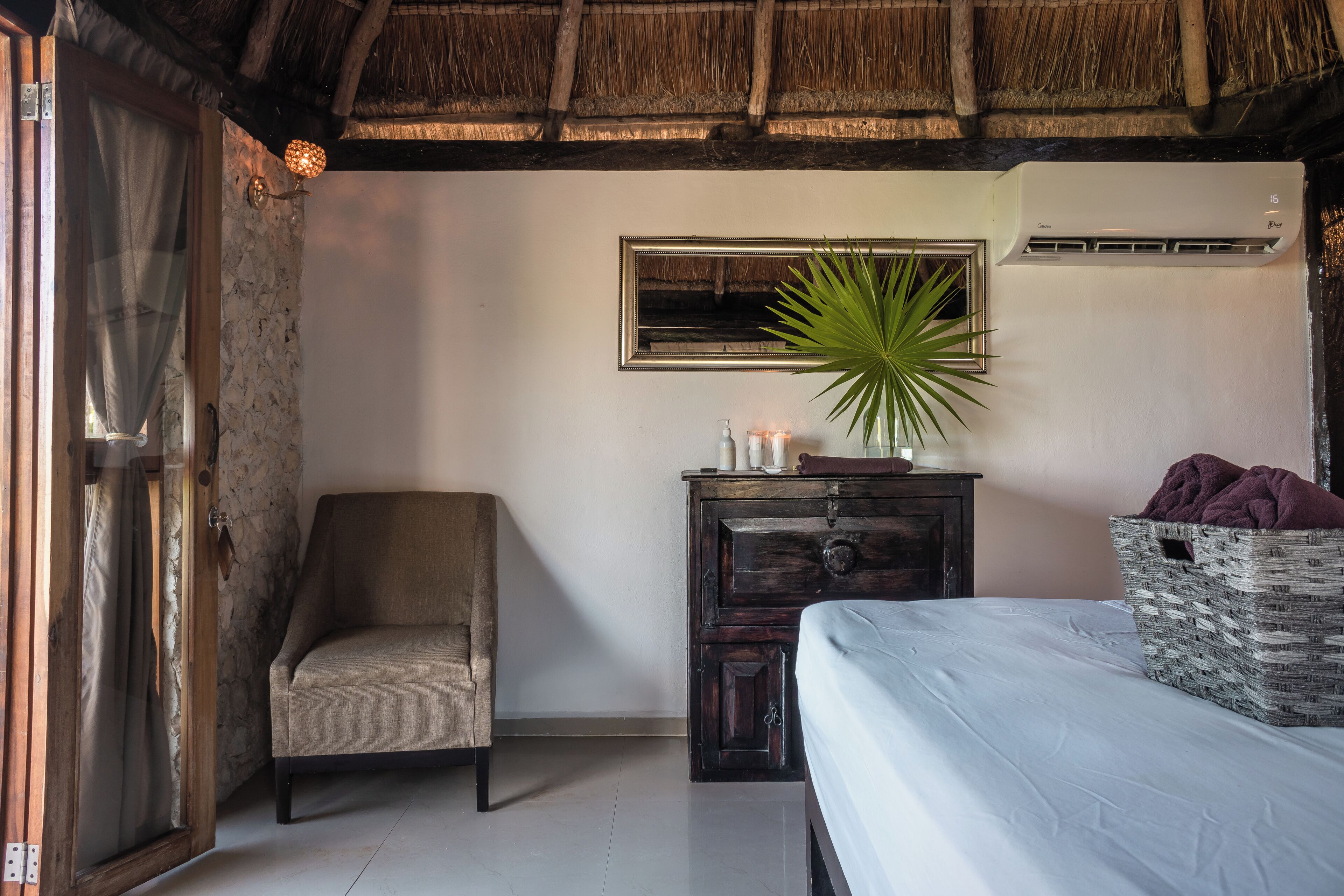 A room with a bed, a chair, a dresser, a mirror, and a potted plant.