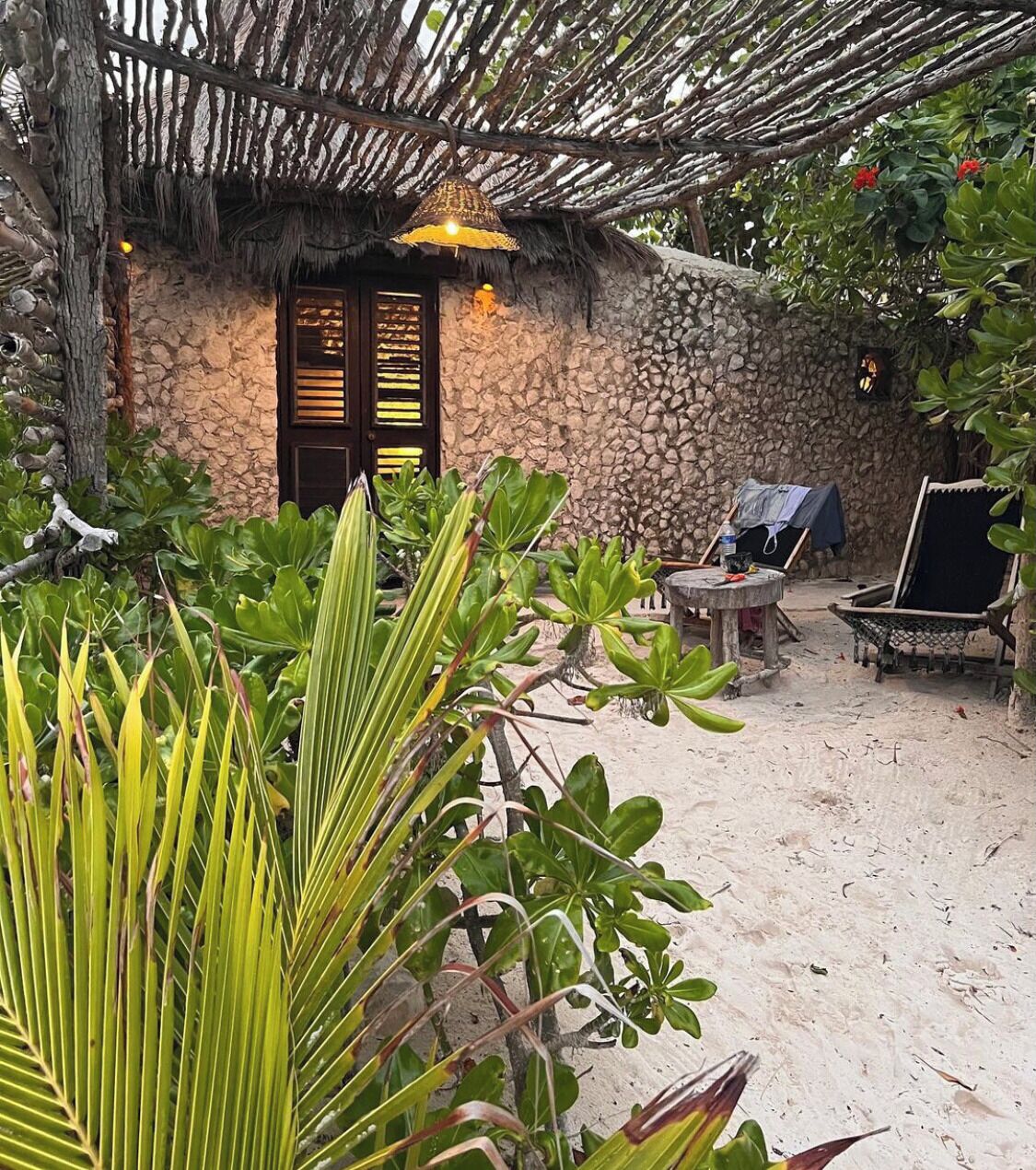 A rustic stone building with a thatched roof, a wooden door, and a small table with a chair.