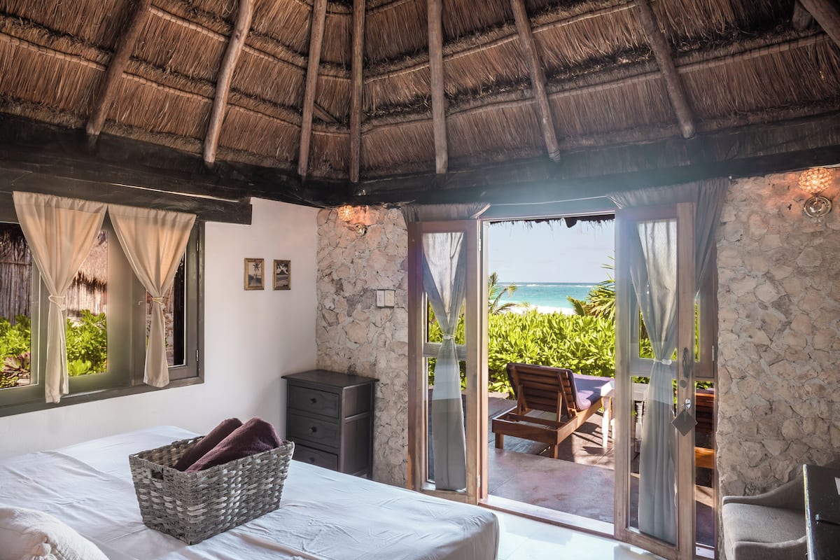 A bedroom with a bed, a wicker basket, a nightstand, and a stone wall.
