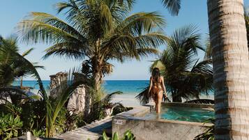 A pool area with a person standing by the edge, surrounded by palm trees and a view of the ocean.
