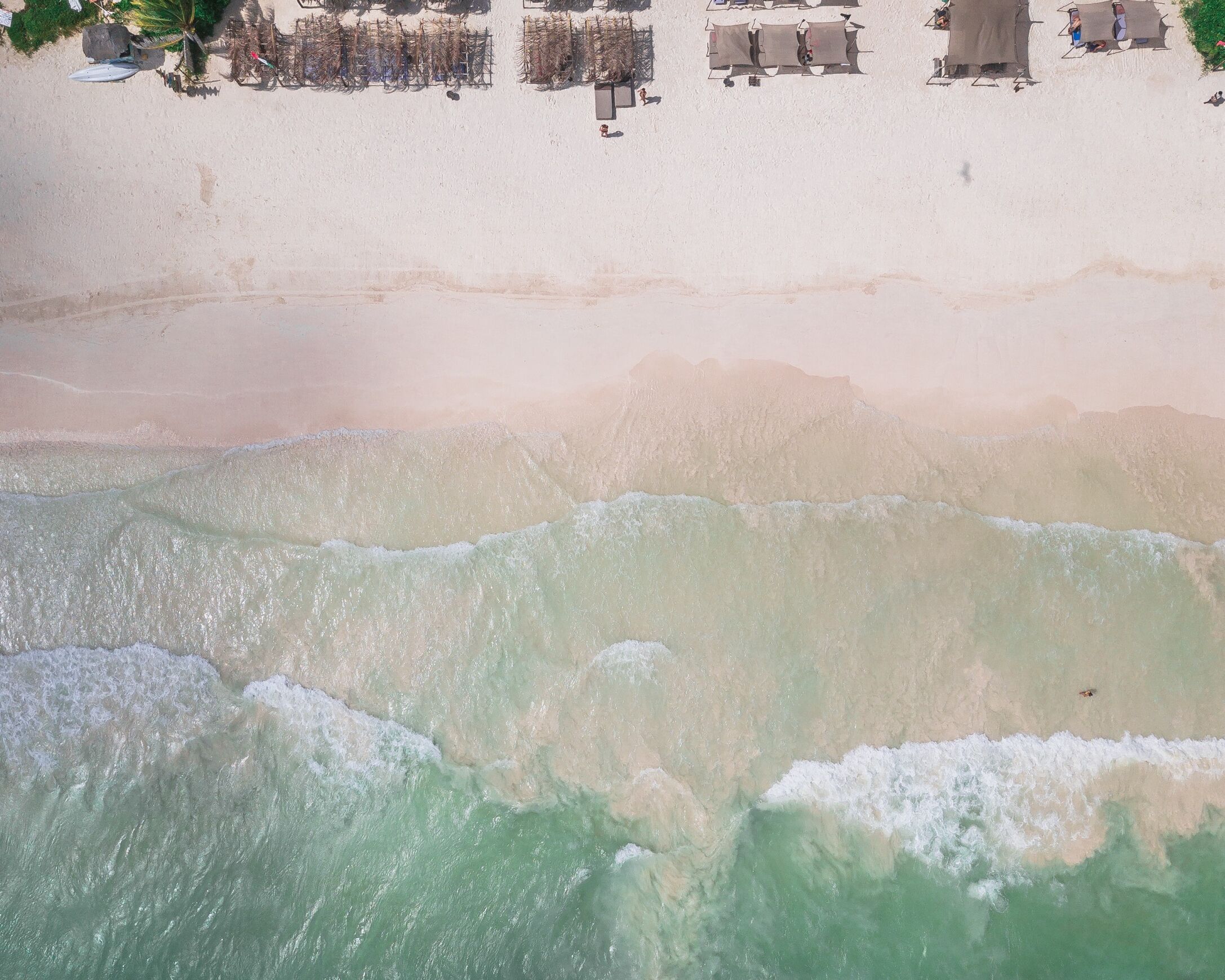 Luchtbeeld van een strand met een rij strandhuisjes en een zandstrand.