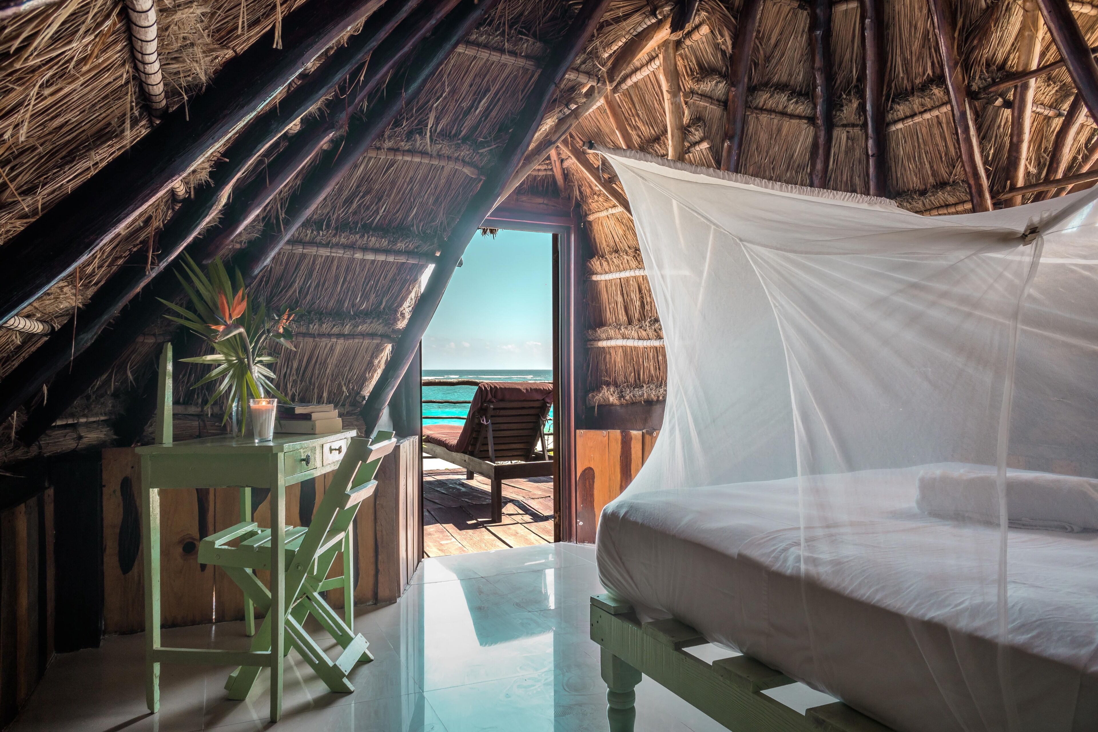 Habitación con cama, una mesa y una silla, y vista a la playa y al océano a través de una puerta abierta.