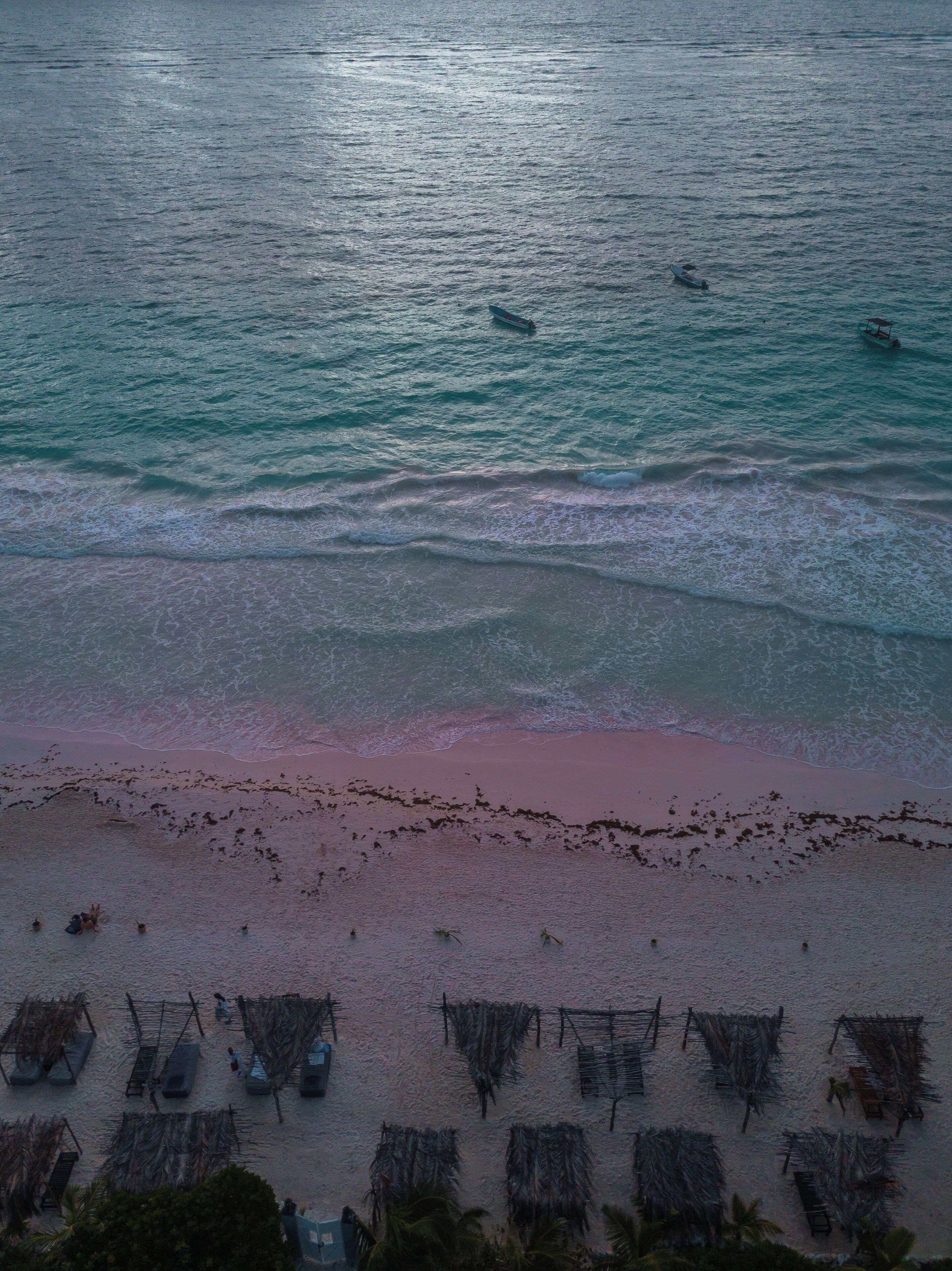 A beach with thatched umbrellas and a few boats in the water.