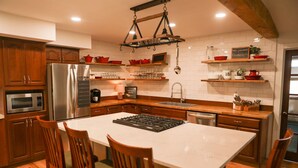 Una cocina moderna con armarios de madera, un refrigerador de acero inoxidable, horno empotrado, una isla grande con estufa a gas y una lámpara colgante.