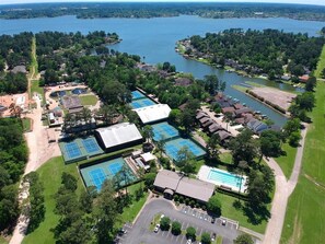 Oversigtsbillede af et boligområde med flere tennisbaner, en swimmingpool og et stort vandområde i baggrunden.
