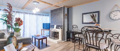 A cozy living room with a fireplace, wooden furniture, and a dining area with metal chairs.