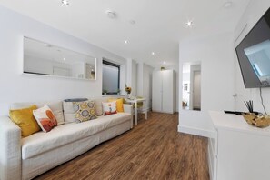 A modern living room with a sofa, a dining table, and a TV mounted on the wall.