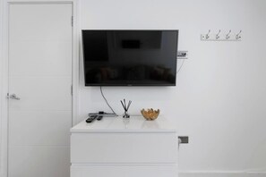 A white cabinet with a television mounted above it, a remote control, and a decorative bowl on the counter.
