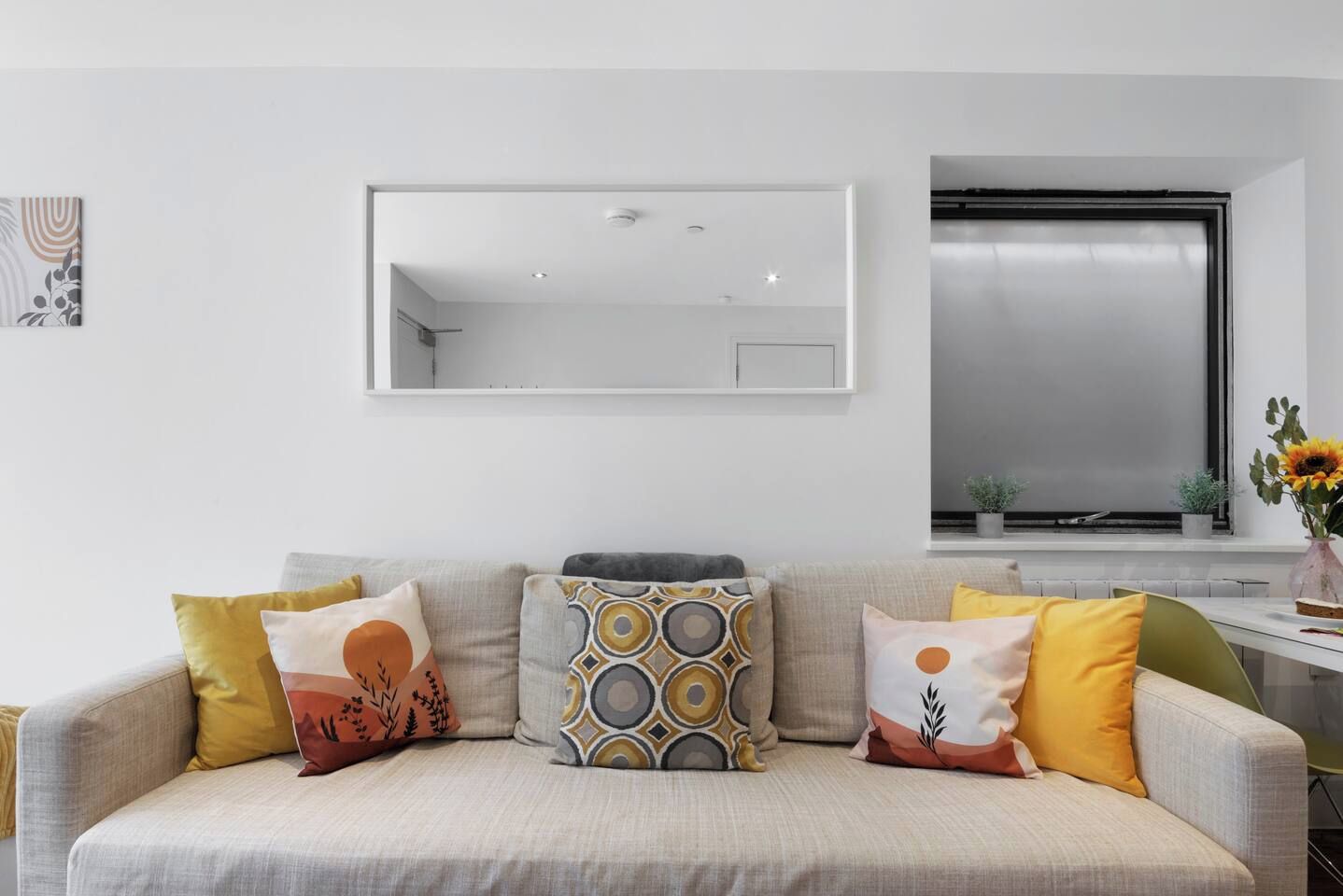 Una sala de estar con un sofá, cojines, un espejo y una ventana con vistas.
