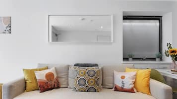 Una sala de estar con un sofá, cojines, un espejo y una ventana con vistas.