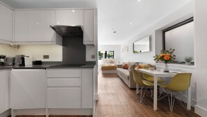 A modern kitchen with white cabinetry, a black range hood, and a dining area with yellow chairs and a white table. - Hermitage Rd N4 🚇 Manor House | Ground floor (London)