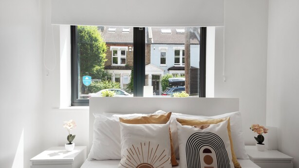 A bedroom with a bed, white bedding, and a window with a view of houses and cars. - Hermitage Rd N4 🚇 Manor House | Ground floor (London)