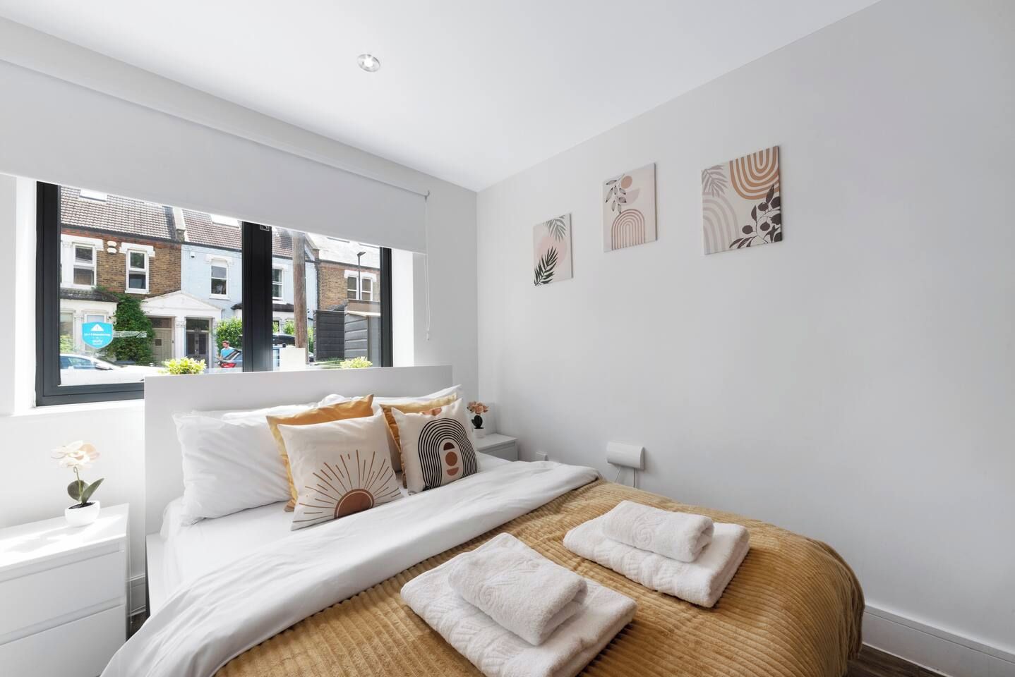 A modern bedroom with a large bed, white bedding, and a view of the street through a window.