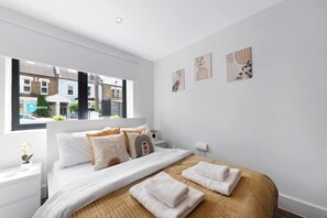 Une chambre à coucher moderne avec un grand lit, du linge de lit blanc et une vue sur la rue par la fenêtre.