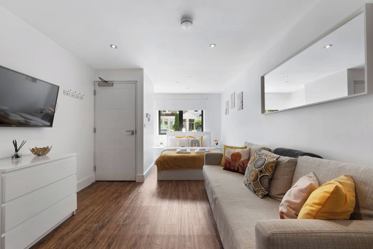 Quarto moderno com cama, sofá, televisão e guarda-roupa branco.